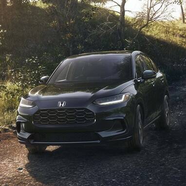 2027 Honda HR-V EX-L in Crystal Black Pearl front view driving on a dirt road in the woods (Subcompact Crossover SUV).